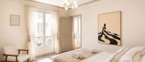 A hotel room with a bed, a chair, a painting, and a view of the outside.