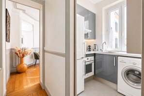 A compact kitchen with a built-in washer, a window, and a vase with dried flowers.
