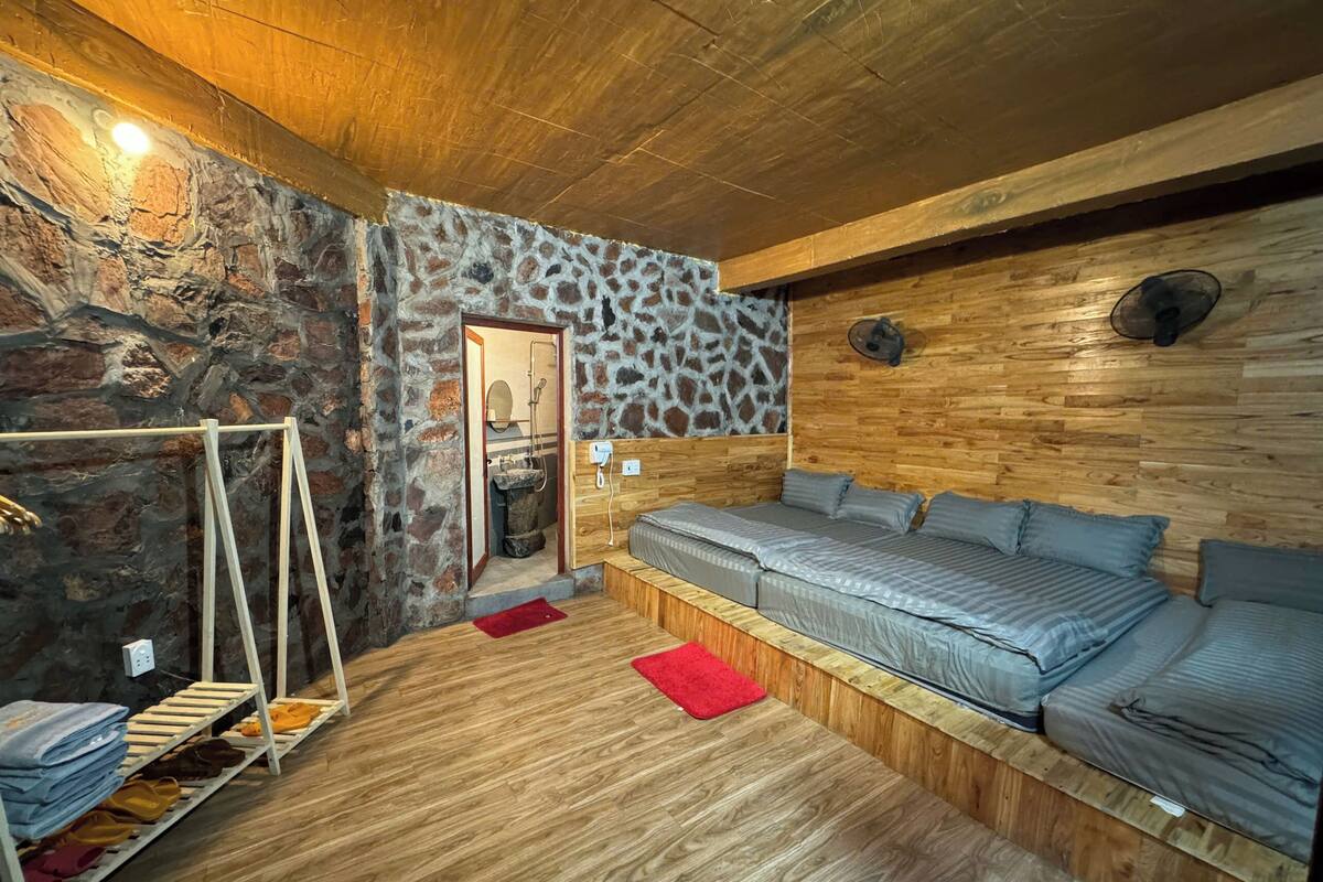 A cozy room with a stone wall, wooden ceiling, and a bed with grey bedding.