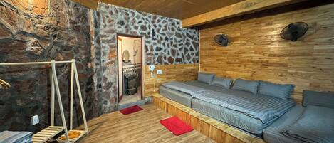 Une pièce chaleureuse avec un mur en pierre, un plafond en bois et un lit recouvert d’une literie grise.
