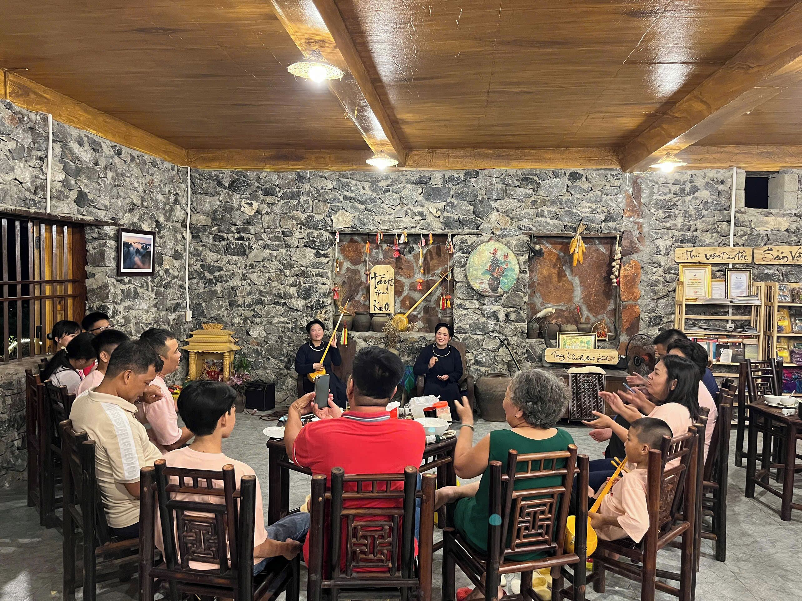 A group of people seated around a table in a room with stone walls and wooden ceiling beams.