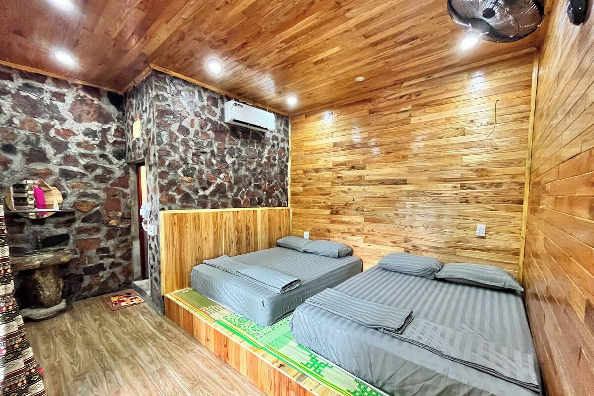 A room with two beds, a stone wall, wooden paneling, and a small shelf with a mirror.