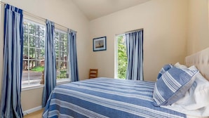 A bedroom with a large bed, two windows with curtains, a small wooden chair, and a framed picture on the wall. - Fairway Paradise | AC, Hot Tub, BBQ (Packwood)