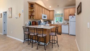 A kitchen with wooden cabinets, a central island with bar stools, a microwave, and a refrigerator. - Fairway Paradise | AC, Hot Tub, BBQ (Packwood)