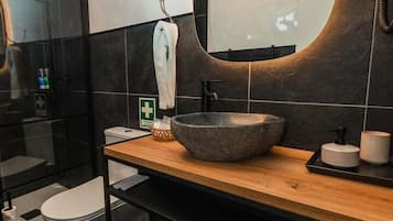 Une salle de bain moderne avec un grand miroir ovale, un meuble-lavabo en bois, un vasque en pierre et un porte-serviettes.