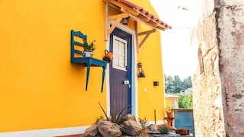 A yellow building with a blue door, a stone oven, and a small garden area.