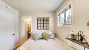 Une chambre à coucher avec un lit, une fenêtre avec des stores, une étagère avec une horloge et une porte donnant sur une autre pièce.