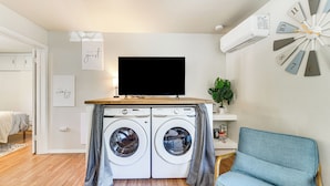 Un espace de vie compact comprenant un lave-linge, un téléviseur et un canapé.
