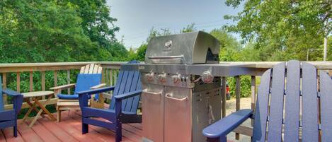 Eine Terrasse mit einem tragbaren Grill, blauen Adirondack-Stühlen und einem Holztisch.