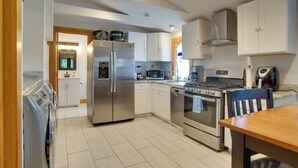 A modern kitchen with stainless steel appliances, a dining area with a wooden table, and white cabinetry. - 1 Mi to Ferry Terminal: Oak Bluffs Family Retreat! (Oak Bluffs)
