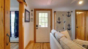 A hallway with a wooden floor, a beige sofa, a white door, and nautical-themed decorations. - 1 Mi to Ferry Terminal: Oak Bluffs Family Retreat! (Oak Bluffs)