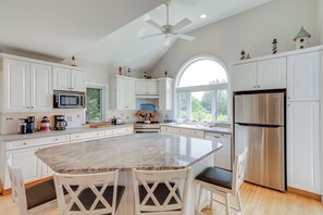 A spacious kitchen with a large island, white cabinetry, stainless steel appliances, and a view of the outdoors.