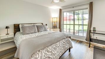 Une chambre à coucher comprenant un lit, un ventilateur de plafond, une table de chevet, une lampe, une fenêtre avec des rideaux et une vue sur l’extérieur.