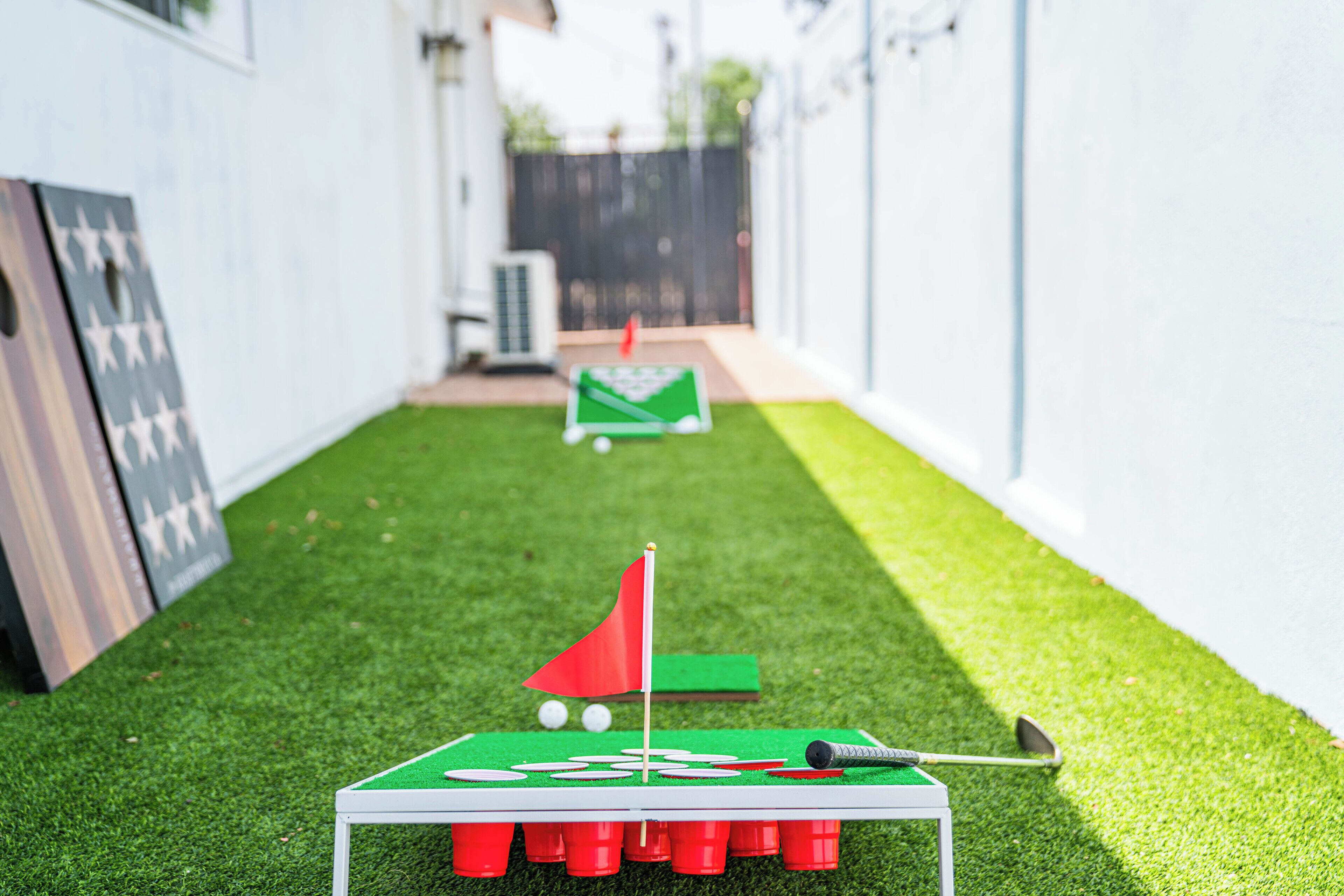 A miniature golf setup with a green mat, red flag, and golf club on artificial grass.