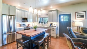 A modern kitchen with stainless steel appliances, a wooden island with bar stools, and a dining area with a dark leather chair. - Missouri River Retreat < 1 Mi to the Water! (Pierre)