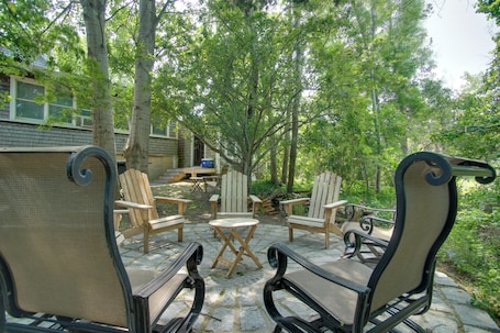 An outdoor seating area with Adirondack chairs and a table, surrounded by trees.
