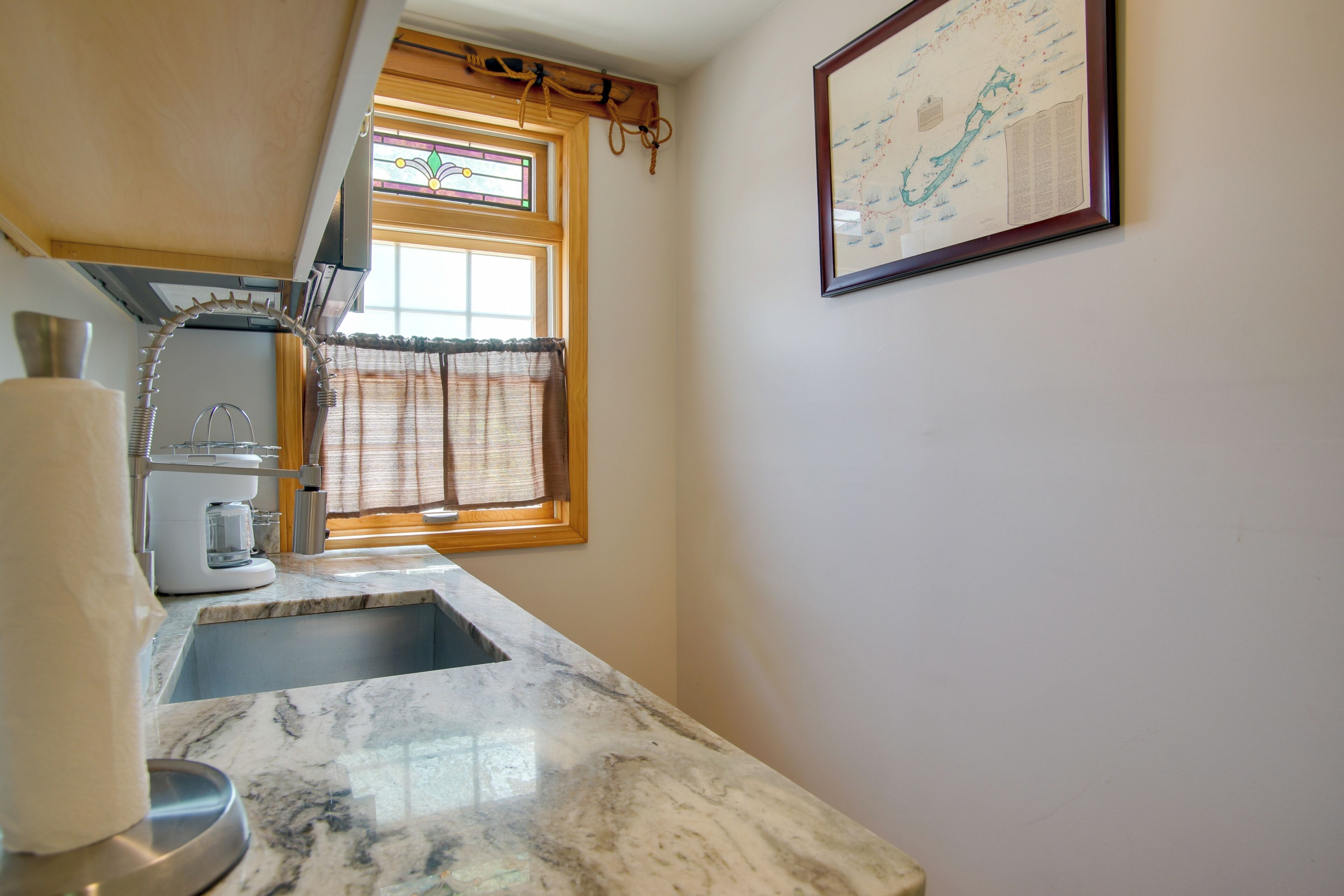 A kitchen with a marble countertop, a coffee maker, and a window with curtains.