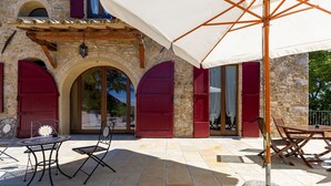 Un patio al aire libre con suelo de piedra, puertas rojas y una mesa con sillas.