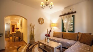 A living room with a sofa, a coffee table, a lamp, a clock, and a window with curtains. - Villa Nikolas - House with pool near Almyrida in Crete (Vámos)