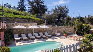 A pool area with lounge chairs and umbrellas, surrounded by stone walls and greenery. - Villa Nikolas - House with pool near Almyrida in Crete (Vámos)