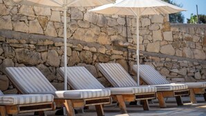 A row of wooden lounge chairs with striped cushions, positioned in front of a stone wall. - Villa Nikolas - House with pool near Almyrida in Crete (Vámos)
