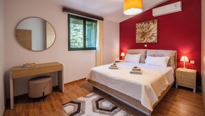 A bedroom with a bed, bedside tables, a desk, a chair, a mirror, a window, and a wall-mounted air conditioner. - Villa Nikolas - House with pool near Almyrida in Crete (Vámos)