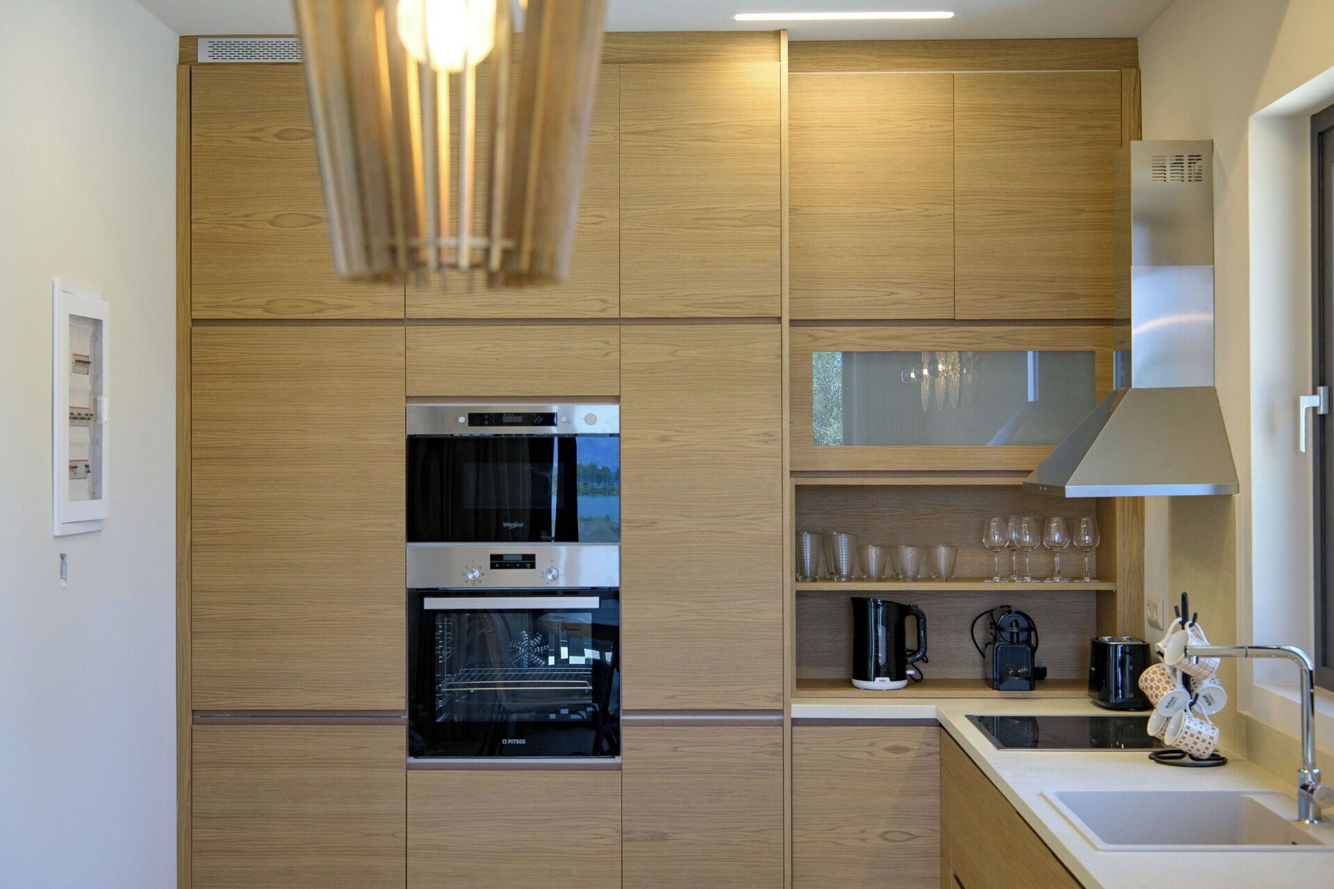 A modern kitchen with wooden cabinets, a built-in oven, a coffee maker, and a sink.