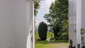 Puerta blanca que da a un área verde con árboles y un muro de piedra.
