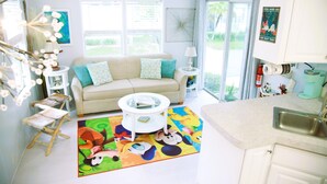 Un salón luminoso con un sofá color crema, una mesita de centro y una alfombra colorida. Se ve un ventanal con vistas a la vegetación.