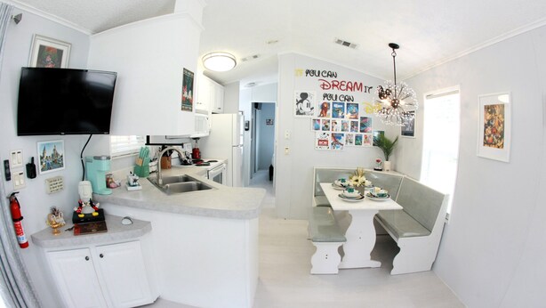 Una cocina compacta con una televisión integrada, una zona de comedor con un banco, y una pared decorada con carteles motivacionales.