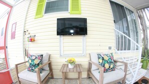 Un área de estar al aire libre con dos sillas de mimbre, una pequeña mesa de madera y un televisor montado en la pared.