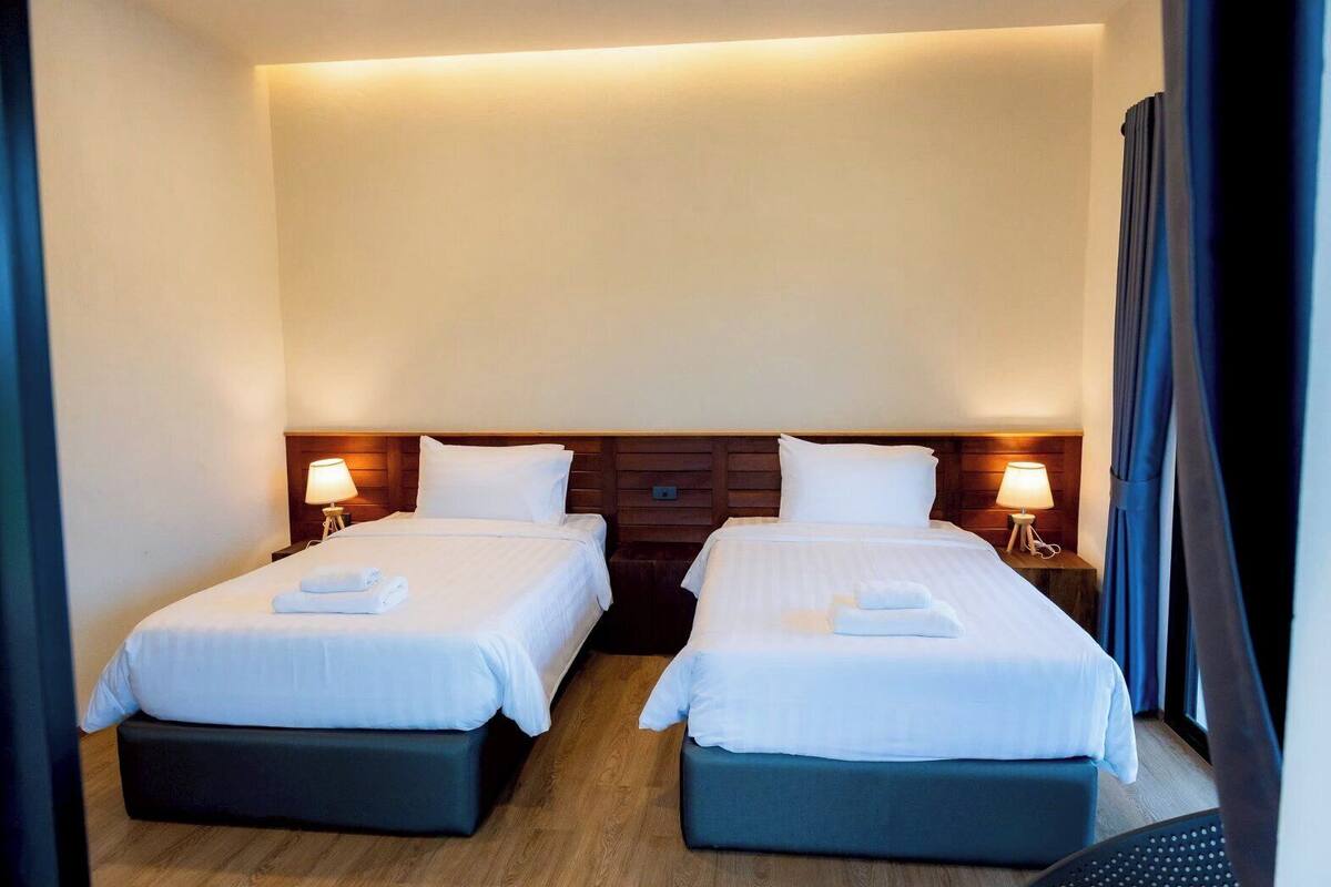 Ein Hotelzimmer mit zwei Einzelbetten, Holz-Kopfteilen, Nachttischlampen und einer dunkel gefärbten Bank.