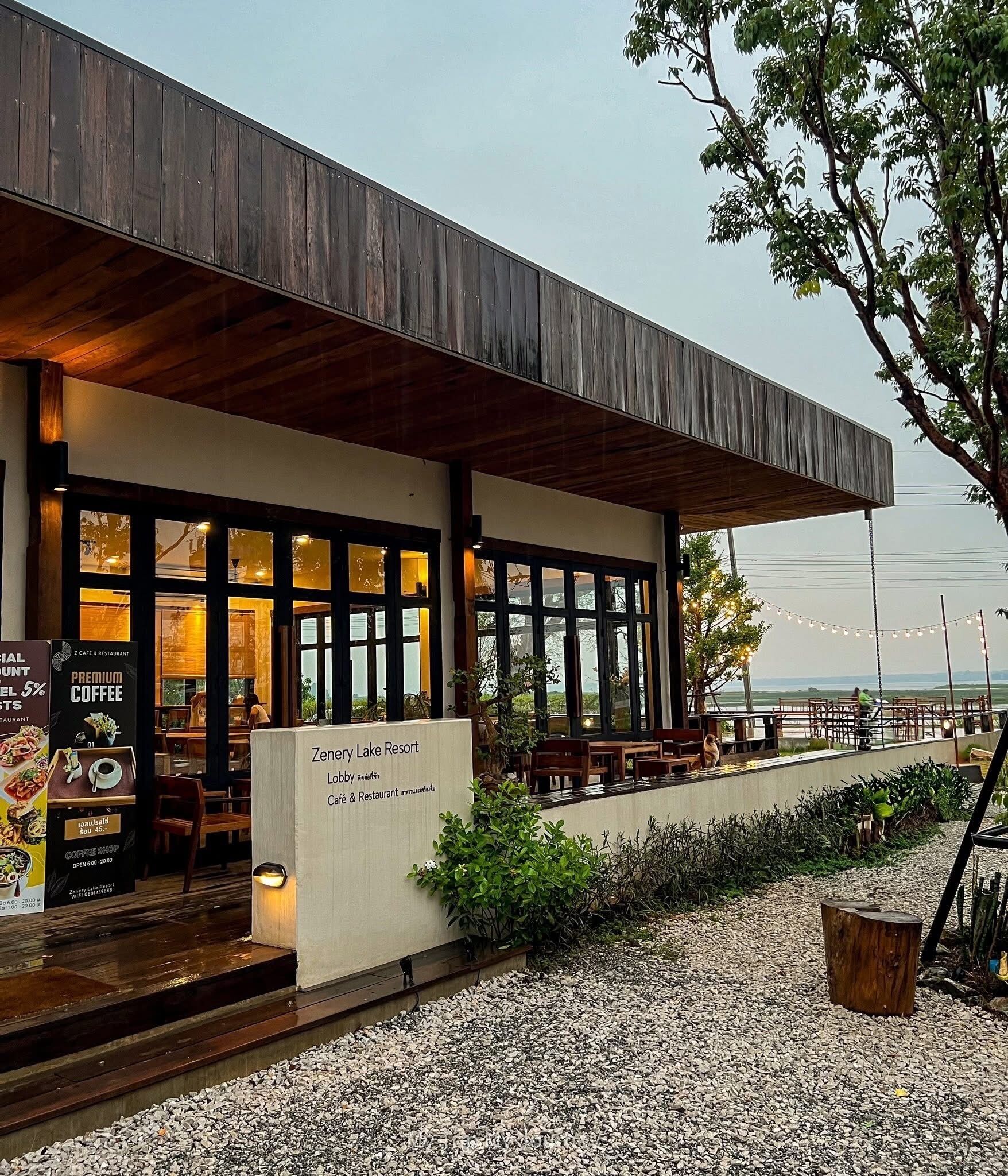 A modern cafe with outdoor seating, a wooden facade, and a view of the beach.