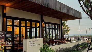 A modern cafe with outdoor seating, a wooden facade, and a view of the beach.