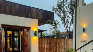 Une entrée moderne avec une porte en bois, une clôture en bambou et des plantes en pot.