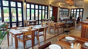Un restaurant avec des tables et des chaises en bois, de grandes fenêtres et un coin bar.