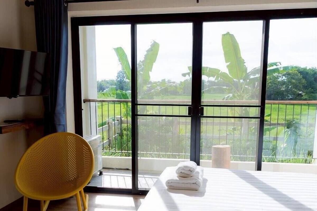 Ein Hotelzimmer mit Bett, Stuhl, Klimaanlage und einem Balkon mit Blick auf Grünflächen.