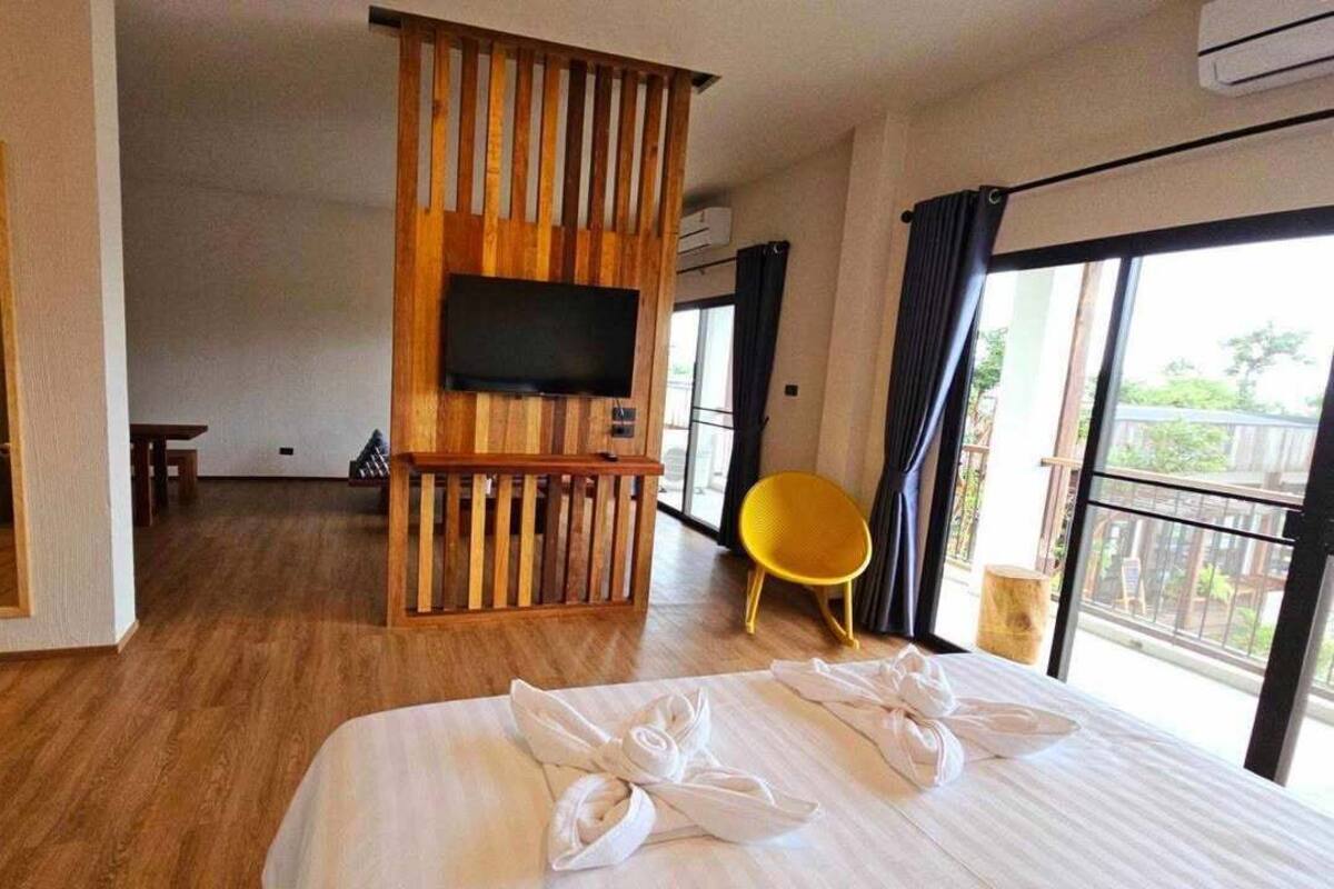 Ein Hotelzimmer mit einem großen Bett, einer Holzwand, einem Flachbildfernseher, einem gelben Sessel und einem Balkon mit Blick.