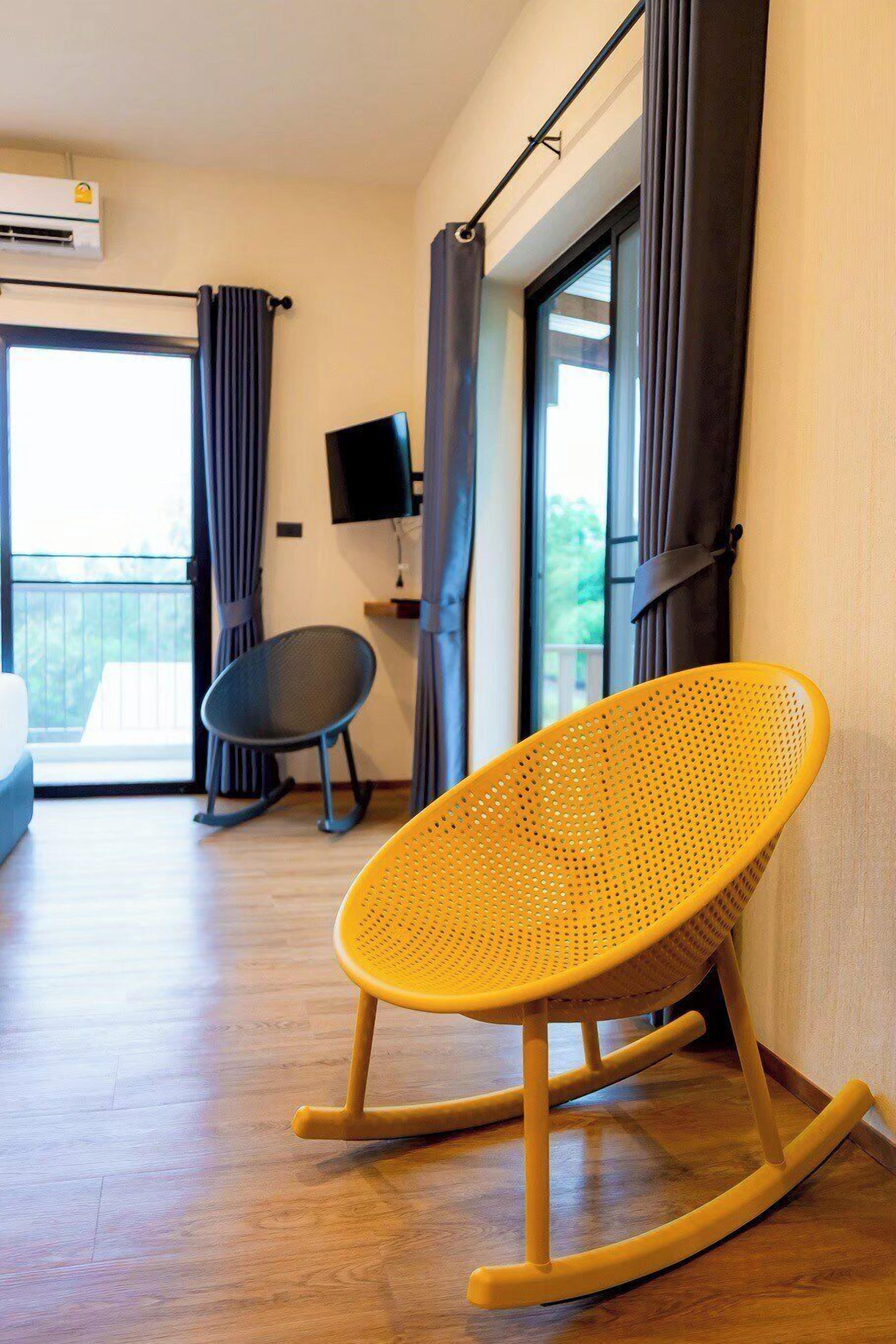 Una habitación con una mecedora, televisión y balcón con cortinas.