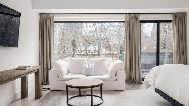 Een moderne hotelkamer met een groot raam, een witte bank, een ronde salontafel en een bed.