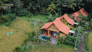 A wooden house with a red roof surrounded by lush greenery and a rice field. - Nava Prana Villa by GenuineHost (Payangan)