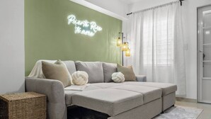 A modern living room with a grey sectional sofa, a green accent wall, and a neon sign. - San Juan Apartament with Beach Access (San Juan)