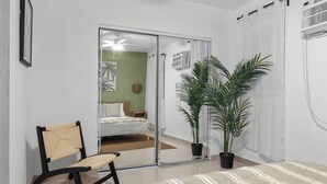 A bedroom with a bed, a chair, a potted plant, and a sliding glass door leading to a bathroom. - San Juan Apartament with Beach Access (San Juan)