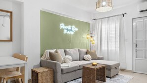 A modern living room with a grey sofa, wicker side tables, a neon sign, and a large window with curtains. - San Juan Apartament with Beach Access (San Juan)