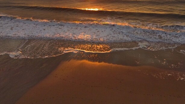 Een strand met golven en een ondergaande zon.