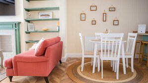 Een woonkamer met een rode bank, witte stoelen, een ronde tafel en een open haard.