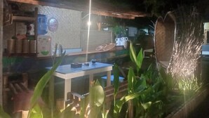 Een terras met een tafel en stoelen, omgeven door planten en een decoratieve lamp.