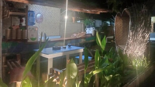 Un espacio exterior para comer con una mesa y sillas, rodeado de plantas y una luz decorativa.