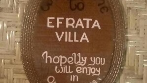 Een rond houten bord met de tekst 'Welkom bij Efrata Villa' en 'Hopelijk zult u het hier naar uw zin hebben.'