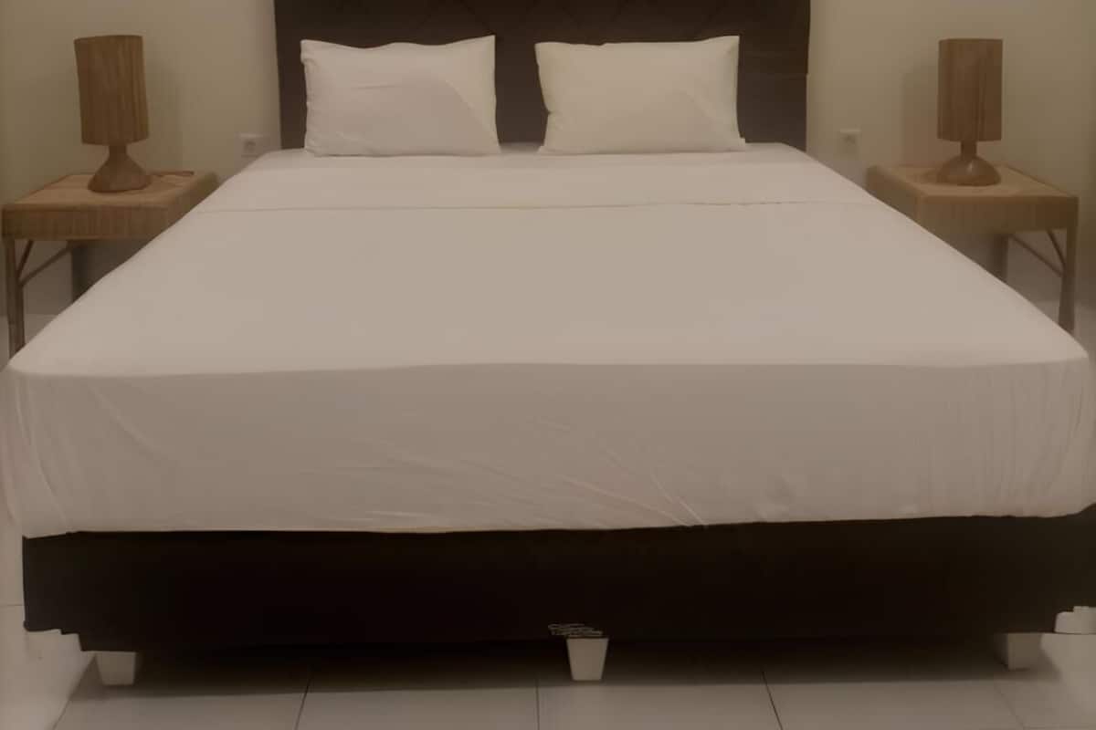 A large bed with a dark headboard, white bedding, and two bedside tables with lamps.